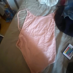 Ljusrosa enkel bodysuit - Säljer en ljusrosa bodysuit med smala axelband och klassisk, enkel design. Modellen är högt skuren vid benen och har en mjuk, stretchig känsla. 