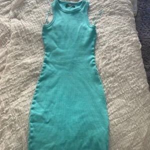 Turkos ribbad klänning från FB Sister - Säljer en tight, ärmlös turkos klänning från FB Sister i ribbad bomull. Klänningen är kort och har en rund halsringning. Perfekt för sommardagar och enkel att styla med sneakers eller sandaler.