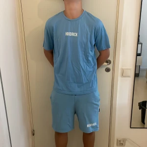 Blå Hoodrich Set M - Snygga ljusblå shorts från Hoodrich med vit logga på vänster ben. Modellen har normal passform, elastisk midja med snörning och två sidofickor. Perfekta för chill eller träning, tillverkade i mjuk bomull för skön känsla. Storlek M