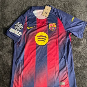 FC Barcelona Raphinha 11 Nike fotbollströja - Snygg FC Barcelona matchtröja med Raphinha 11 på ryggen, tillverkad av lätt polyester. Tröjan har klassiska blå och röda vertikala ränder, gula detaljer och klubbmärke på bröstet. Champions League-patch på ärmen och Spotify-logga på framsidan.
