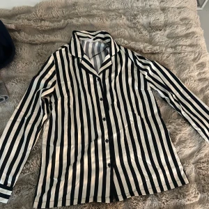 Randig skjorta från Serenity S - Aldrig använda men super fint och hjärtligt sett. Kommer både byxor och skjorta. Snygg skjorta från Serenity i svart och vitt med vertikala ränder. Skjortan har klassisk krage, knäppning framtill och långa ärmar. Materialet är glansigt och känns mjukt mot huden, perfekt för en chill och stilren look. 🥰🥰