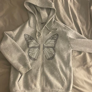 Grå hoodie med fjärilstryck - Grå hoodie med dragkedja och stor glittrig svartvit fjäril på framsidan. 💙