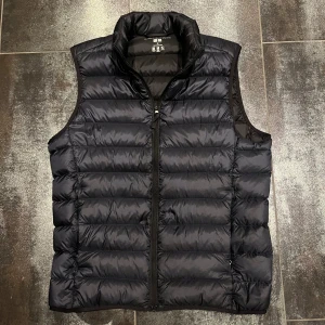 Svart dunväst från Uniqlo - Säljer en marinblå, quiltad dunväst från Uniqlo Ultra Light Down. Västen är lätt, har dragkedja framtill och levereras med en smidig förvaringspåse. Perfekt för lager-på-lager och enkel att ta med sig. Klassisk passform och stilren look. Nästan oanvänd