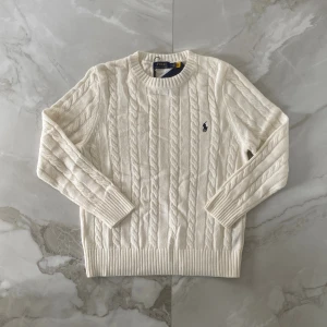 Ralph Lauren Stickad Tröja - Stickad vit tröja från Polo Ralph Lauren med klassisk rund halsringning och broderad marinblå logga på bröstet. Tröjan är i mjuk bomull och har ribbade muddar vid ärmslut och nederkant. Perfekt för en clean och stilren look. Tröjan passar som S även om det står M. Den är helt ny och om ni har frågor så är det bara att skriva😊