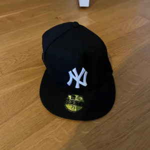 New Era Yankees 59FIFTY svart keps - Svart New Era 59FIFTY keps med klassiskt New York Yankees broderi framtill i vitt och World Series 2000 patch på sidan. Rak skärm, grå undersida och gul storleksdekal kvar på skärmen. Perfekt för dig som gillar streetwear och sport.