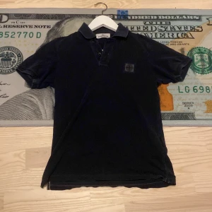 Mörkblå Stone Island Junior piké - Säljer en mörkblå pikétröja från Stone Island Junior. Klassisk krage, det är bra skick bara två mini hål som ni ser på bild 4 (inget som märks) killen på bild 3 är 170 och sitter bra (passar dig som är 160-170) det kommer med en extra knapp! Hör av dig vid minsta fundering !
