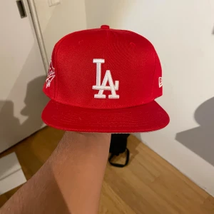 Röd LA Dodgers 59FIFTY keps New Era - Har 3 till färger då jag råkade köpa fel storlek. Helt nya Snygg röd LA Dodgers 59FIFTY keps från New Era med vit broderad LA-logga framtill och 1988 World Series patch på sidan. Klassisk flat brim och MLB-logga bak. Tillverkad i 100% polyester, perfekt för dig som gillar streetwear och sportig stil.