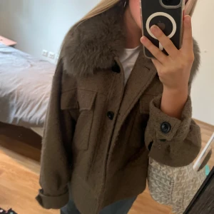 Brun Meotine jacka med stor pälskrage - Säljer en brun jacka med oversized passform och stor fluffig pälskrage. Jackan har stora fickor framtill, knappar och långa ärmar med breda muddar. Perfekt för dig som vill ha en mysig och trendig look i höst och vinter.
