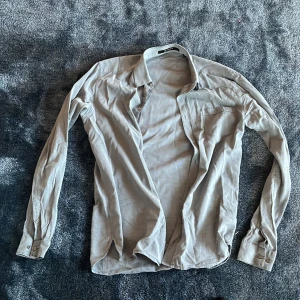 Grå skjorta från Tiger of Sweden - Snygg grå skjorta från Tiger of Sweden i klassisk modell med lång ärm och bröstficka. Skjortan har knappar vid ärmslut och en stilren krage. Perfekt för dig som gillar en clean och enkel look.