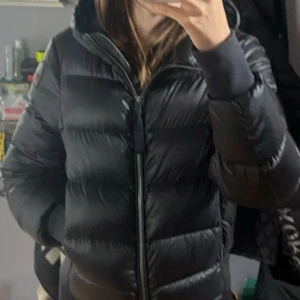 Svart pufferjacka Parajumpers  - Säljer en svart pufferjacka från Parajumpers, modell Sheen. Jackan har en glansig finish, huva och dragkedja framtill. Klassisk patch på ärmen och ribbade muddar vid handlederna. Perfekt för kalla dagar. Nypris 6200kr