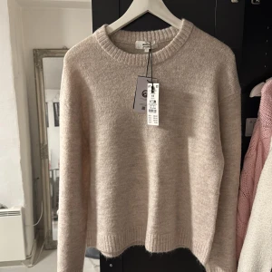 Beige stickad tröja från Gina  - Mysig beige stickad tröja från Gina med rund halsringning och ribbade muddar. Tröjan har en enkel och stilren design, perfekt för lager-på-lager och chill dagar. Långärmad och i mjukt material som känns skönt mot huden. Säljer denna då jag råkat beställa en lika som jag redan har, oanvänd