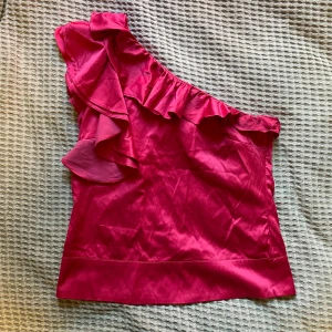 Rosa topp - Jättesnygg rosa topp med volang. Offshoulder på ena armen. Ser lika dan ut på baksidan av tröjan som på framsidan 🩷