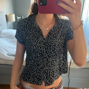 Prickig svart blus  - Svart kortärmad skjorta från H&M Divided med vita prickar, klassisk krage och knappar framtill. 