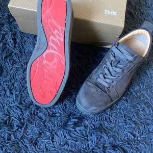 Christian Louboutin skor  - Snygga mörkgrå sneakers i mocka från Christian Louboutin med ikonisk röd sula och diskret snörning. Skorna har en stilren design med rund tå och platt sula, perfekta för dig som vill sticka ut med exklusiva detaljer. alla tillbehör medföljs. Säljer eftersom de ej kommer till användning, köpte på vinted i våras så de är lite använda men de är äkta, kvitto finns (se sista bild)