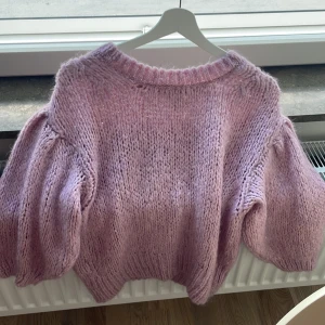 Ljuslila stickad tröja River Island - Superfin stickad tröja från River Island i en mjuk ljuslila ton. Tröjan har puffiga långärmar och grovstickad struktur som ger en cozy vibe. Perfekt för dig som gillar volym och vill ha en trendig look med extra statement på ärmarna.