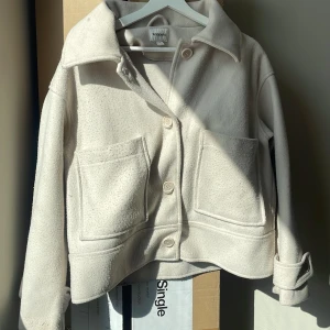Beige jacka från Kappahl, M - Säljer en beige jacka från Kappahl i storlek M. Jackan har två stora fickor framtill, klassisk krage och stängs med knappar. 