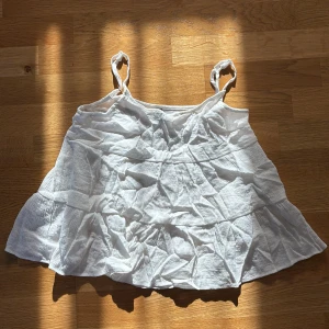 Vit volangig linnetopp med axelband - Säljer en vit linnetopp med tunna axelband och volangig, luftig design. Toppen är ärmlös och har en lätt rynkad struktur i tyget som ger en chill och somrig vibe. Perfekt för varma dagar och enkel att matcha med jeans eller shorts.