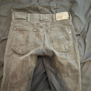 Replay svarta jeans, W30 L32 - Svarta Replay jeans med klassisk femficksdesign och snygga broderade bakfickor. Jeansen har normal passform och raka ben. Tillverkade i slitstarkt jeanstyg med Replay-logga på bakfickan och läderpatch i midjan. Perfekta för en stilren och avslappnad look.