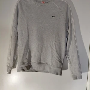 Grå sweatshirt från Lacoste - grå sweatshirt från Lacoste med rund hals och logga på bröstet. Storlek S. Använd men har inga eventuella skador eller fläckar. 