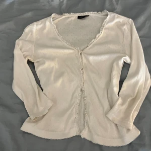 Vit blus med spetskant från Lindex - Söt vit blus från Lindex med små diskreta hålmönster, v-ringning och fina spetsdetaljer längs kanterna. Blusen har knappar framtill och trekvartsärm. Perfekt att slänga över en topp för en romantisk look. Strl 38 men sitter som xs/s