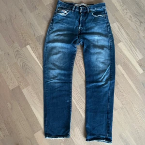 Blå Diesel jeans med slitna detaljer - Snygga blå jeans från Diesel med slitna detaljer vid fickorna och klassisk femficksdesign. Jeansen har en rak passform och tydliga slitningar för en cool, avslappnad look. Märkespatch bak i midjan och diskret tvättad effekt på benen. OBS! (Inner längd 76cm)