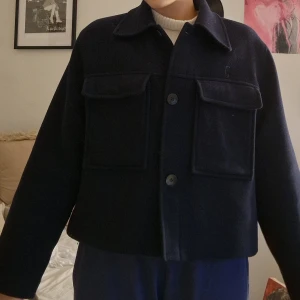 Kort kappa i marin blå - Säljer en mörkblå kort kappa  med stora bröstfickor och knappar framtill. Jackan har lite croppad passform och klassisk krage. Från Carin Wester, köpt på Åhléns. Inga defekter, det är bara lite små "hår" från stickad tröja på baksidan på bilden, går enkelt att ta bort!