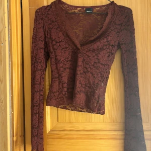 Vinröd spetsblus från Gina Tricot - Säljer en vinröd långärmad blus från Gina Tricot i storlek XS. Toppen är helt i spets med blommigt mönster och har v-ringning. Den är figurnära och genomskinlig, perfekt att styla med ett linne under eller som den är för en cool look.