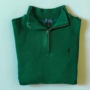 Grön stickad tröja Polo Ralph Lauren Quarter zip 1/4 - Snygg grön stickad tröja från Polo Ralph Lauren med half zip och hög krage. Tröjan har långärmade ärmar och klassisk broderad logga på bröstet. Perfekt för dig som gillar stilrena och tidlösa plagg med en sportig touch. Storlek S (Står L men är åldrarna 14-16, därav passar den S). Tredje bilden visar bäst hur färgen ser ut i verkligheten.
