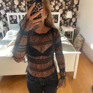 Svart meshblus med prickigt mönster XS - Säljer en transparent svart meshblus från Holly & White  på Lindex i storlek XS. Blusen har lång ärm, prickigt mönster och volangdetaljer längs ärmar och kropp. Perfekt att styla med ett snyggt linne eller bh under för en trendig look.