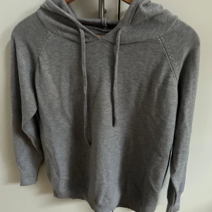 Grå hoodie med huva och snörning - Skit snygg Kashmir tröja som passar perfekt till hösten eller under en väst. Storleken är 160-170 och skulle säga att den är mer åt det mindre hållet och den har aldrig varit använd så den är i utmärkt skick