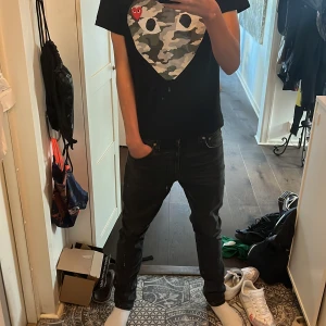 Svarta Nudie Jeans - Säljer ett par svarta jeans från Nudie Jeans med klassisk femficksdesign och diskret tvättad look. Jeansen har raka ben och slim passform, med snygga detaljer på bakfickorna och en liten logotyp. Jävligt sköna. Köpta för 1600 på Åhléns, har kvitto. W29 L32. Är lite större i midjan