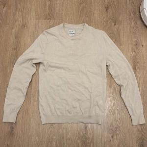 Beige stickad tröja från these glory days - En stilren beige stickad tröja från these glory days med rund halsringning och långa ärmar. Tröjan har en klassisk passform och är tillverkad i mjukt material som passar perfekt för lager-på-lager under kyligare dagar.