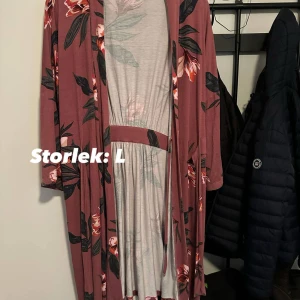 Blommig långklänning i vinrött strl: L - Superfin långklänning i vinröd nyans med stora blommor i rosa, vitt och grönt. Klänningen har lång ärm, markerad midja och fickor i sidorna. Mjuk och skön i ett stretchigt material, perfekt för dig som gillar en avslappnad men snygg look. 