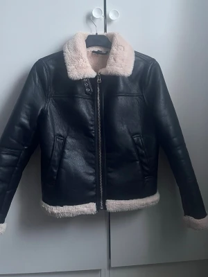 Black teddy jacket with faux fur - Säljer en svart teddyjacka med mjukt, ljust fuskpälsfoder och krage. Jackan har dragkedja framtill, två fickor och detaljer i skinnimitation. Perfekt för kalla dagar och ger en cool vibe till din outfit.