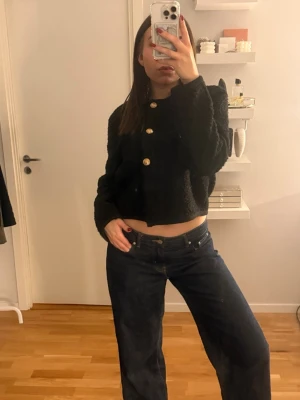 Svart croppad kofta med guldknappar - Säljer en svart, croppad kofta med stora guldknappar framtill. Koftan har lång ärm och är gjord i ett mysigt, stickat material som känns fluffigt. Perfekt för dig som vill ha en trendig och bekväm look. Det är en knapp som har gått av, där av är det tre knappar istället för 4. Inget som syns och är fortfarande en fin tröja 💓