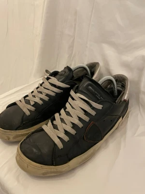 Philippe Model svarta sneakers i skinn - Svarta sneakers från Philippe Model med vita snören och vit sula. Skorna är i skinn och har en klassisk låg profil med rund tå och diskret logga på sidan. Perfekta för en avslappnad och trendig look.