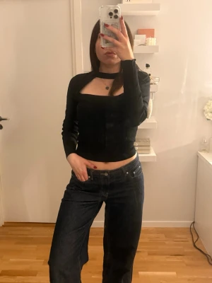 Svart croppad långärmad topp - Säljer en svart croppad topp med lång ärm och unik cut-out detalj vid halsen. Toppen har en tight passform och är perfekt för att lyfta en outfit. Materialet känns mjukt och stretchigt, vilket gör den bekväm att bära. Från Zara i storlek M