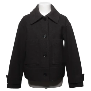 Svart kappa med stora fickor - Säljer en svart ulljacka med klassisk krage och stora framfickor. Jackan har knäppning med stora knappar framtill och justerbara detaljer vid ärmsluten. Perfekt för dig som gillar en enkel men stilren look.