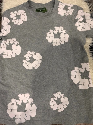  Denim Tears - Snygg grå t-shirt från Denim Tears med vita blomtryck. Använd endast ett par gånger, mycket bra skick.  Storlek S, men sitter lite oversized/baggy. Jag är 175 cm / 70 kg och den passar helt okej med avslappnad passform.  Inga fläckar eller hål. Skickas snabbt 📦 