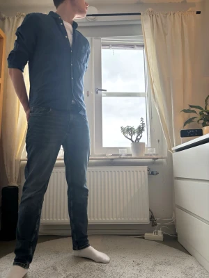 Mörkblå skjorta med knappar - Säljer en mörkblå skjorta i bomull med klassisk krage och knappar framtill. Skjortan har lång ärm och en bröstficka på vänster sida. Passformen är normal och tyget känns mjukt och skönt mot huden. Perfekt att bära över en t-shirt.