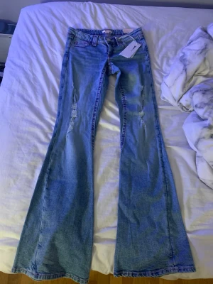 Lågmidjade bootcut jeans med rosa broderi - Säljer ett par blå bootcut jeans från Gina i storlek XS. Jeansen har detaljer framtill och snyggt rosa broderi på bakfickorna. Säljer pga att dem inte passar.