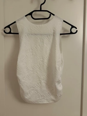 Vit ärmlös linnetopp med strukturmönster - Säljer en vit ärmlös linnetopp med lite schrunch vid sidorna. Perfekt att styla med jeans eller kjol för en fräsch look.