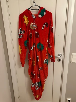 Röd julig byxdress från Silly Santa - Mysig röd byxdress med julmönster från Silly Santa. Motiv av pepparkakor, polkagrisar, julkulor och kransar. Perfekt för att maxa julkänslan. 