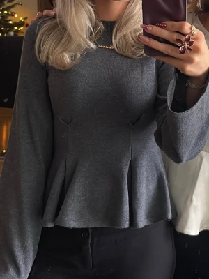 Mörkgrå stickad tröja - Mörkgrå stickad tröja från Gina Tricot med peplumskärning och långa större ärmar. Tröjan har rund halsringning och är i mjukt material som sitter snyggt på kroppen och tajtare i midjan. Använd endast en gång så är i nyskick utan prislapp kvar😇