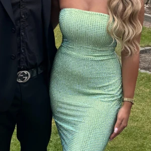 Ljusgrön glittrig axelbandslös klänning - Säljer en superfin ljusgrön axelbandslös klänning med glittriga stenar över hela tyget. Klänningen är figurnära och har en snygg, tight passform som framhäver midjan. Perfekt för dig som vill sticka ut och glänsa på nästa event!