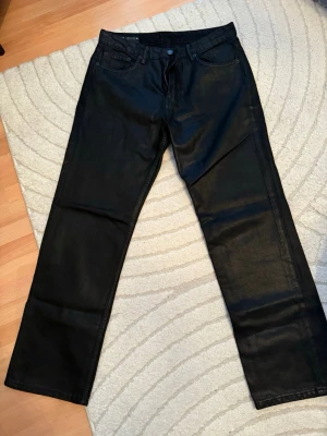 Svarta raka byxor från Zara - Säljer ett par svarta byxor från Zara med rak passform och klassisk femficksdesign. Byxorna har en snygg, lite glansig finish som ger en cool look. Materialet känns som en blandning av bomull och syntet, vilket gör dem både bekväma och stilrena.