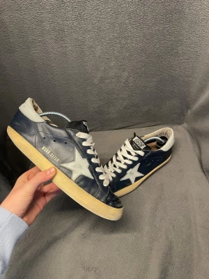 Golden Goose - Snygga mörkblå sneakers från Golden Goose med vit stjärndetalj på sidan i storlek 40 men passar 41. Nypris runt 6000. Skorna har tecken på användning då en av skadorna är ett hål i sulan. Perfekt för sommarn, höst och vår. Super för dig som vill ha en stilren look tilll vardagen.          Skriv vid frågor, priset är inte hugget i sten🤝