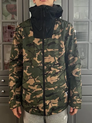 Camouflagemönstrad skidjacka från Wearcolour. Stl M - Säljer en camouflagemönstrad skidjacka från Wesrcolour. Jackan har svart huva och dragkedja framtill. Jackan har långa ärmar med muddar, justerbar huva med snörning, snölås och praktiska fickor med dragkedja. Perfekt för skidåkning eller på fritiden. Jackan har aldrig använts utan är i nyskick. Personen på bilden är 186 cm lång.