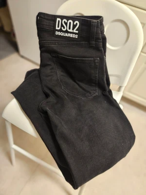 Svarta jeans från Dsquared2 - Säljer ett par svarta jeans från Dsquared2 med coola färgstänk på framsidan. Jeansen har klassisk femficksdesign, raka ben och normal passform. Tillverkade i slitstarkt bomullsmaterial och har snygga detaljer som metallnitar och bälteshällor.
