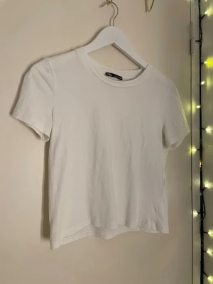 Vit basic t-shirt från Zara - Enkel och stilren vit t-shirt från Zara i mjuk bomull. Modellen är kortärmad med rund halsringning och har en lite kortare passform. Säljer då jaf aldrig använder denna.